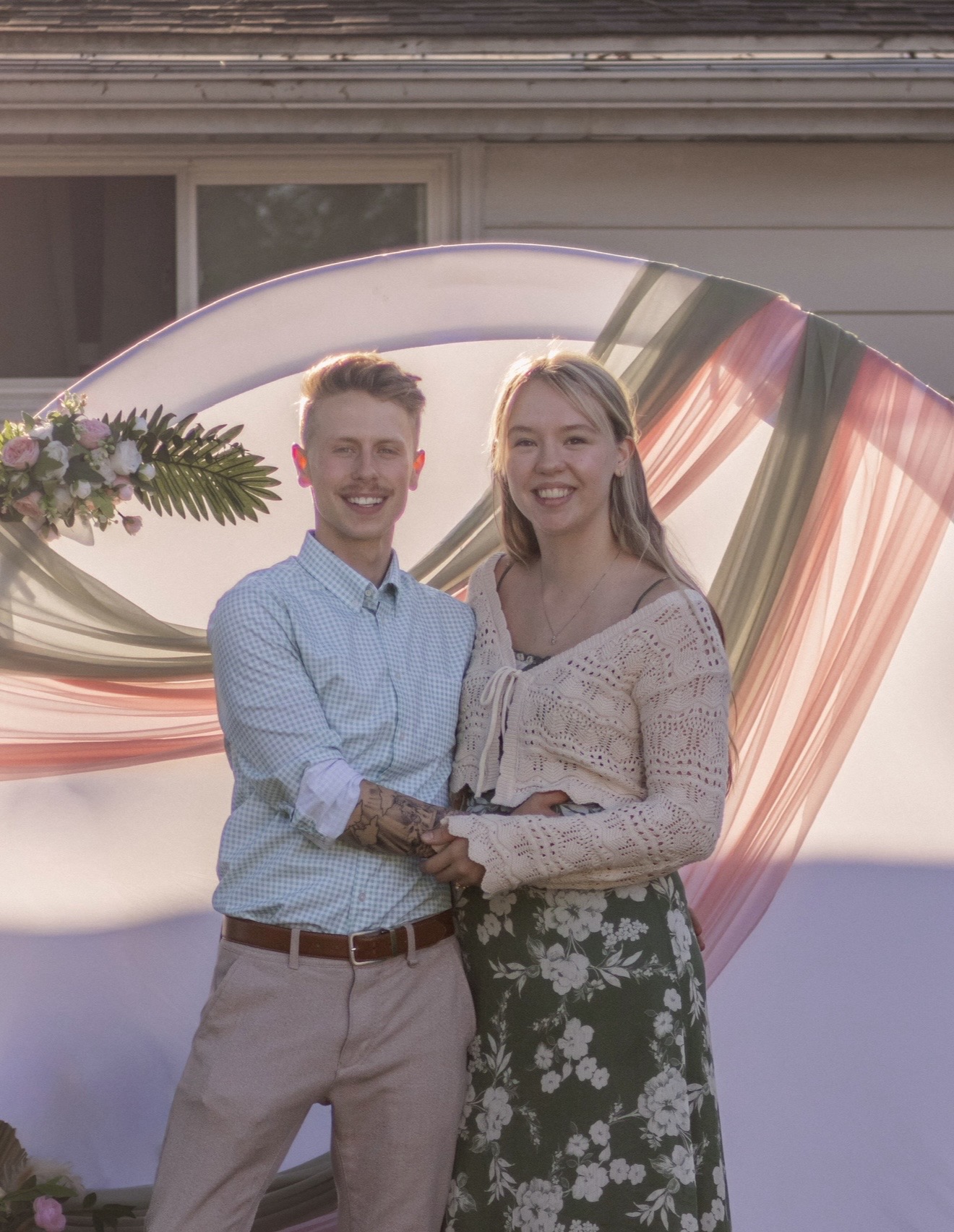 Logen and Chelsey smiling in front of a floral arch at sunset